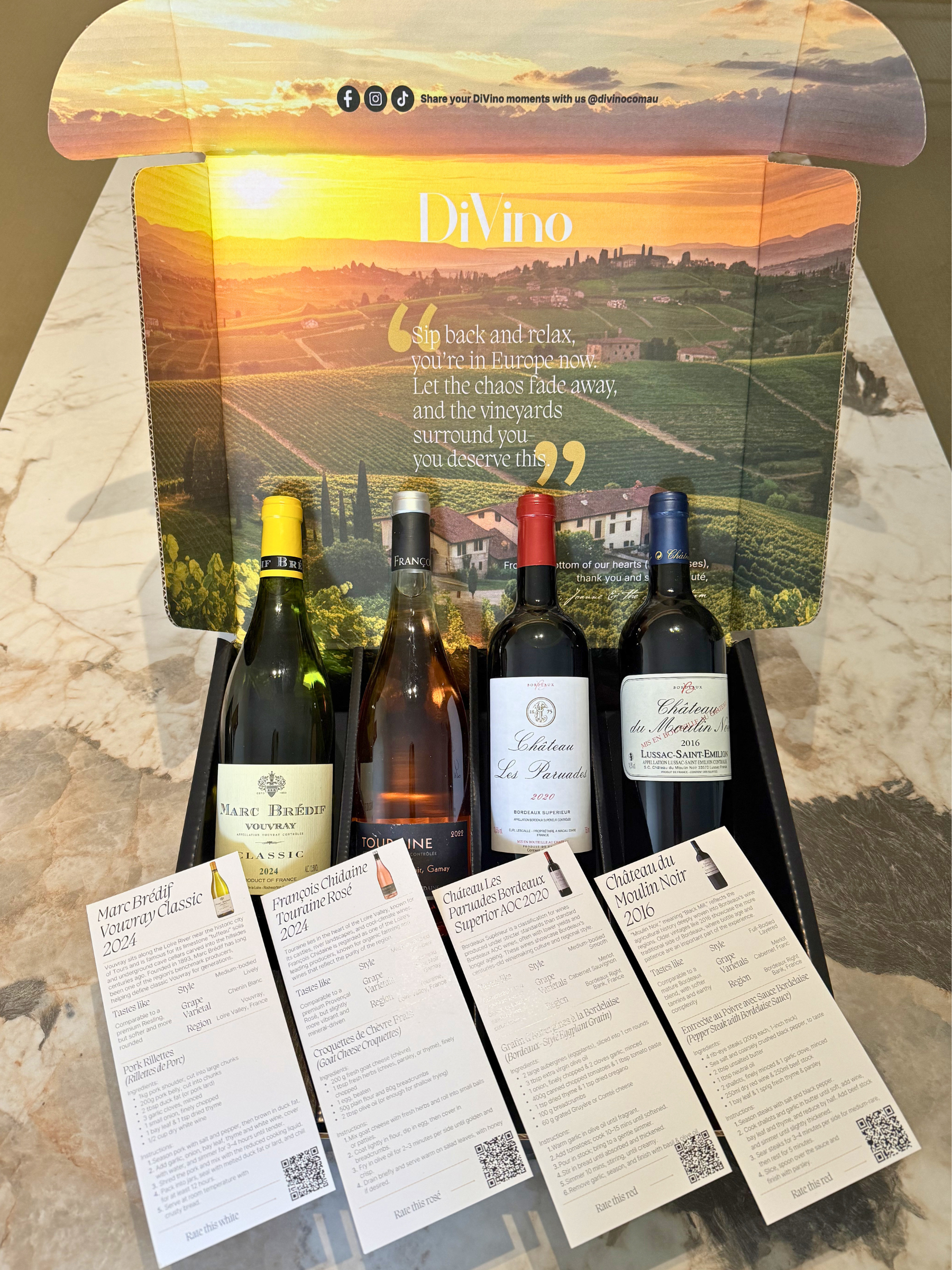 Five bottles from The Grand Tour by DiVino.com.au are displayed in a black box with an Italian vineyard scene inside the lid, each with a wine info card, evoking curated elegance—all presented on marble. - DiVino.com.au